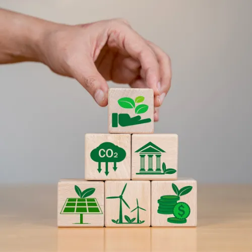 Main empilant des cubes en bois avec des icônes CO2, énergie solaire, éolienne et finance verte illustrant le bilan carbone