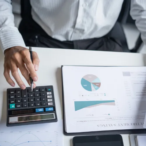 Personne calculant le coût d'une certification RSE avec une calculatrice et des graphiques financiers