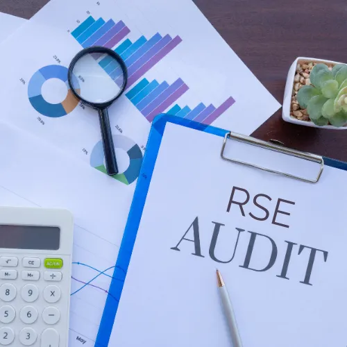 Classeur avec l'inscription "RSE Audit" posé sur un bureau avec loupe, calculatrice et graphiques