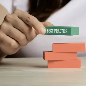 Main posant un bloc vert "Best Practice" sur une pile de blocs orange illustrant les bonnes pratiques ISO 14001