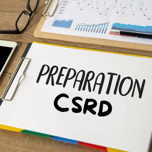 Classeur avec l'inscription "Préparation CSRD" sur un bureau avec graphiques et lunettes illustrant la préparation à la directive européenne