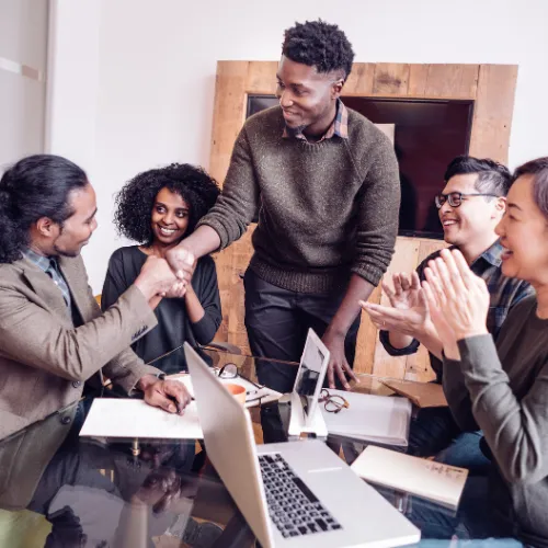 Équipe multiculturelle et diverse célébrant un succès autour d'une table avec ordinateurs portables