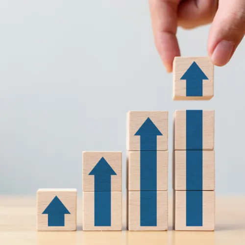 Main empilant des cubes en bois avec des flèches bleues vers le haut symbolisant la progression des points de durabilité et du score RSE