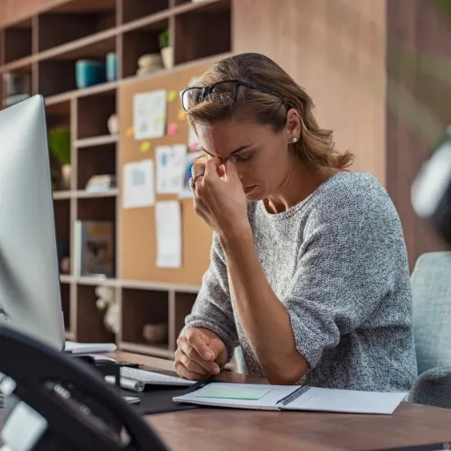 Femme stressée tenant ses lunettes devant son ordinateur illustrant la difficulté d'obtenir une certification RSE sans accompagnement