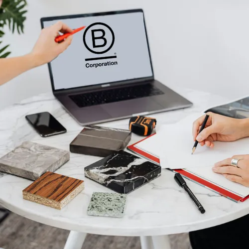 Deux personnes travaillant sur une table blanche avec un ordinateur affichant le logo B Corporation pour préparer une certification