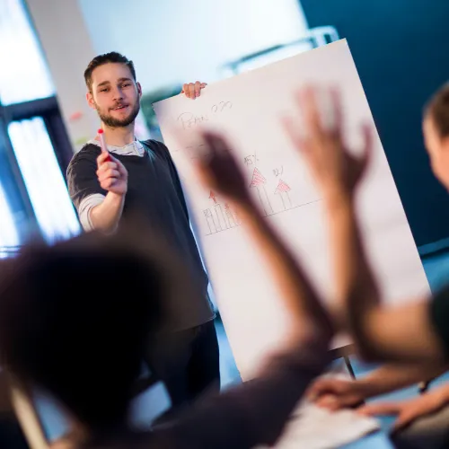 Formateur RSE tenant un panneau devant un groupe de participants avec des mains levées lors d'une session de formation sur les niveaux EcoEntreprise